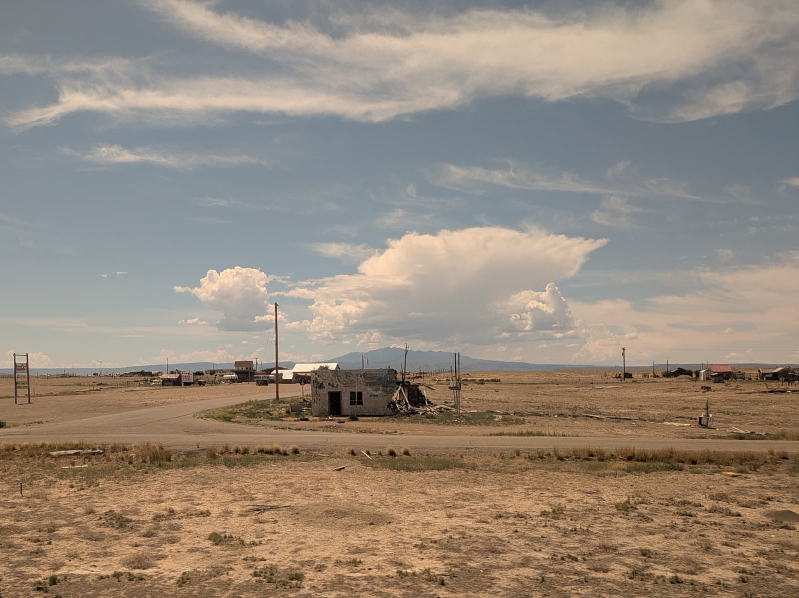 A lone ruined building on bare desert ground under big clouds