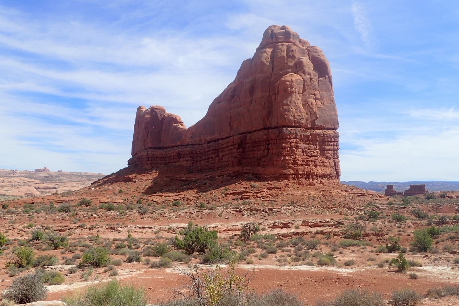 A tall red sandstone tower over desert scrub under a blue sky