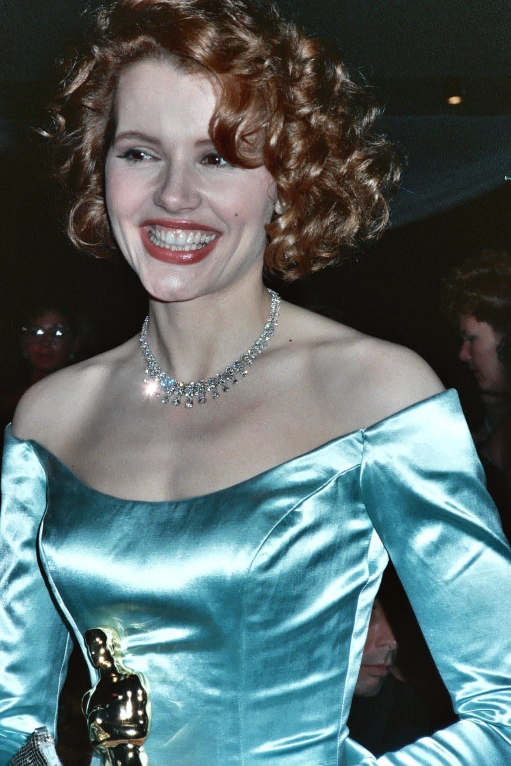 Geena Davis laughing in a pale blue satin gown and diamond necklace