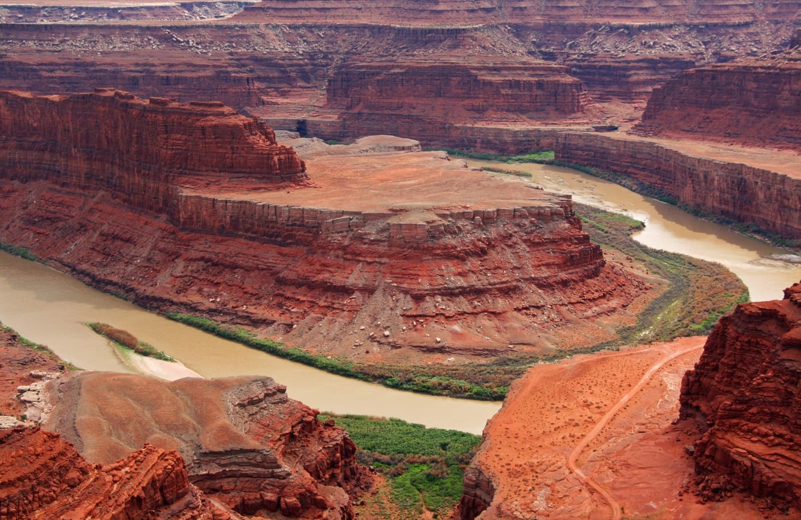 A deep red canyon with the river bending round a sandstone tongue far below