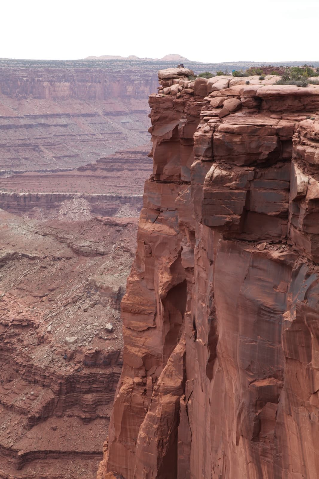 A vertical red sandstone cliff edge with canyon country falling away behind