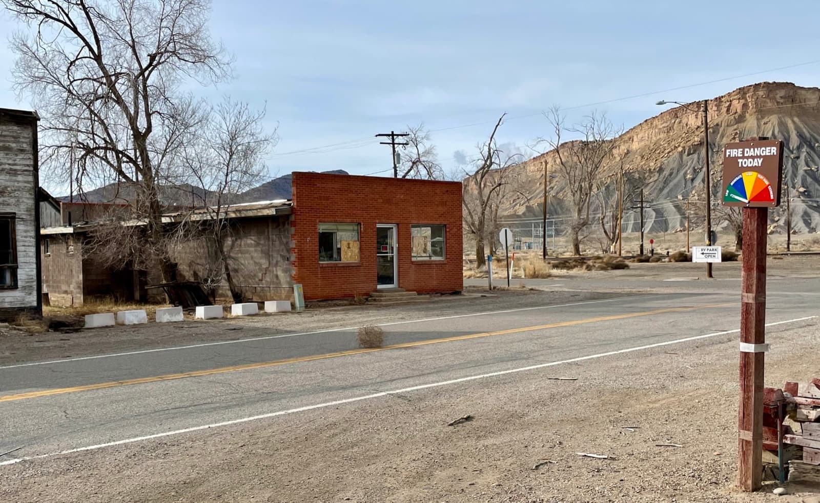 A shut-up brick building and a bare tree on a quiet road under grey cliffs
