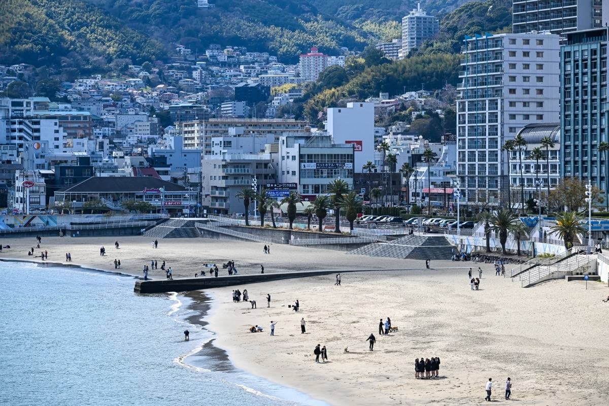 A curved sandy beach below hotels climbing a green hillside