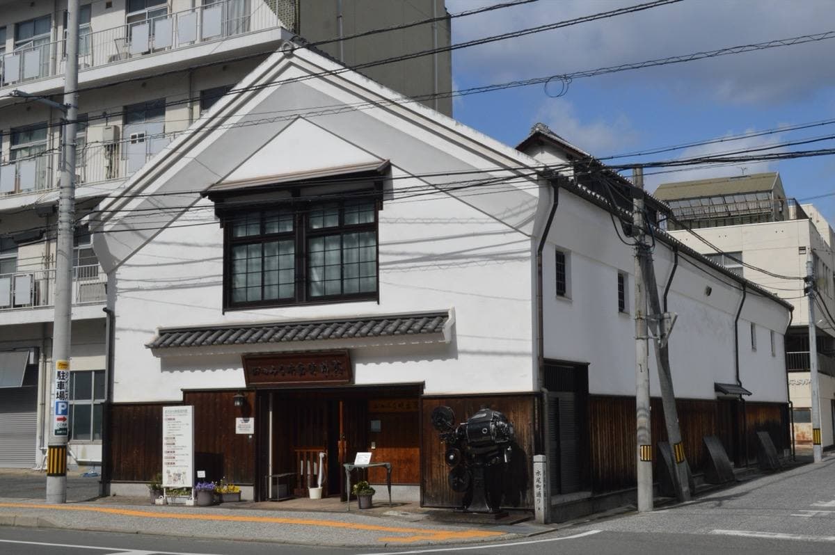 A white-walled storehouse with a black-tiled roof on a street corner
