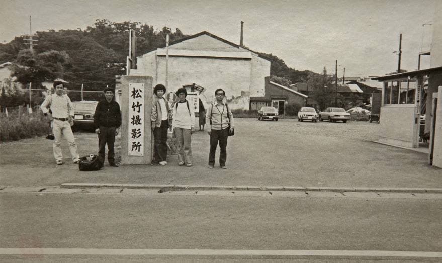 People pose by a studio gatepost with a signboard