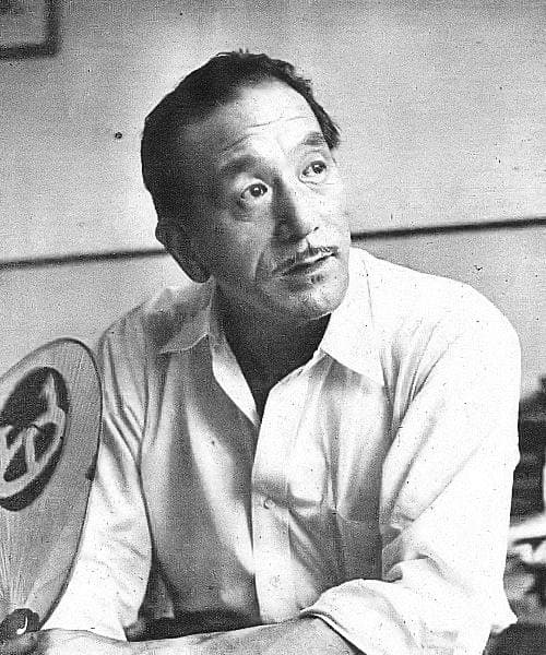 Yasujirō Ozu in an open-necked shirt, a round fan beside him