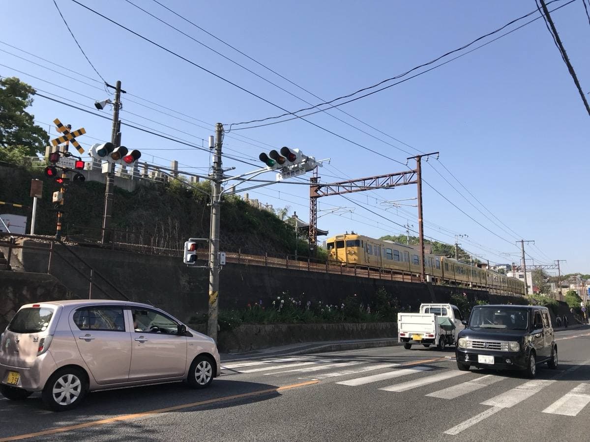 A local train passes behind a level crossing on a hillside street