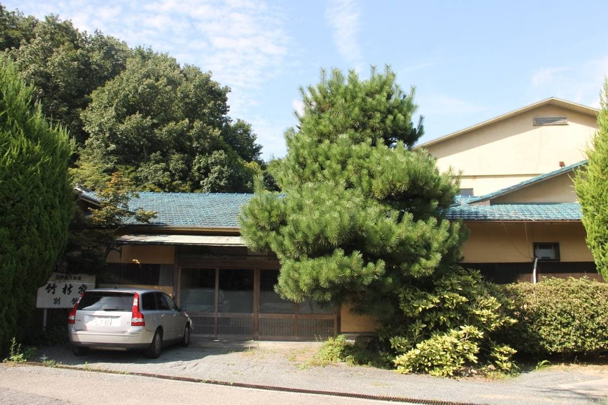 A low Japanese inn behind pine trees and a gravel forecourt