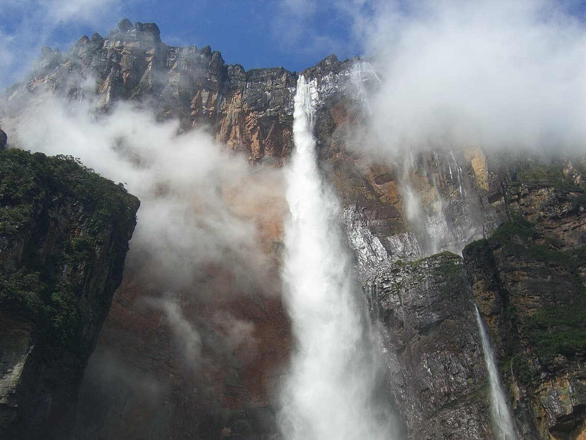 A tall, thin waterfall falling from the edge of a dark flat-topped mountain into cloud