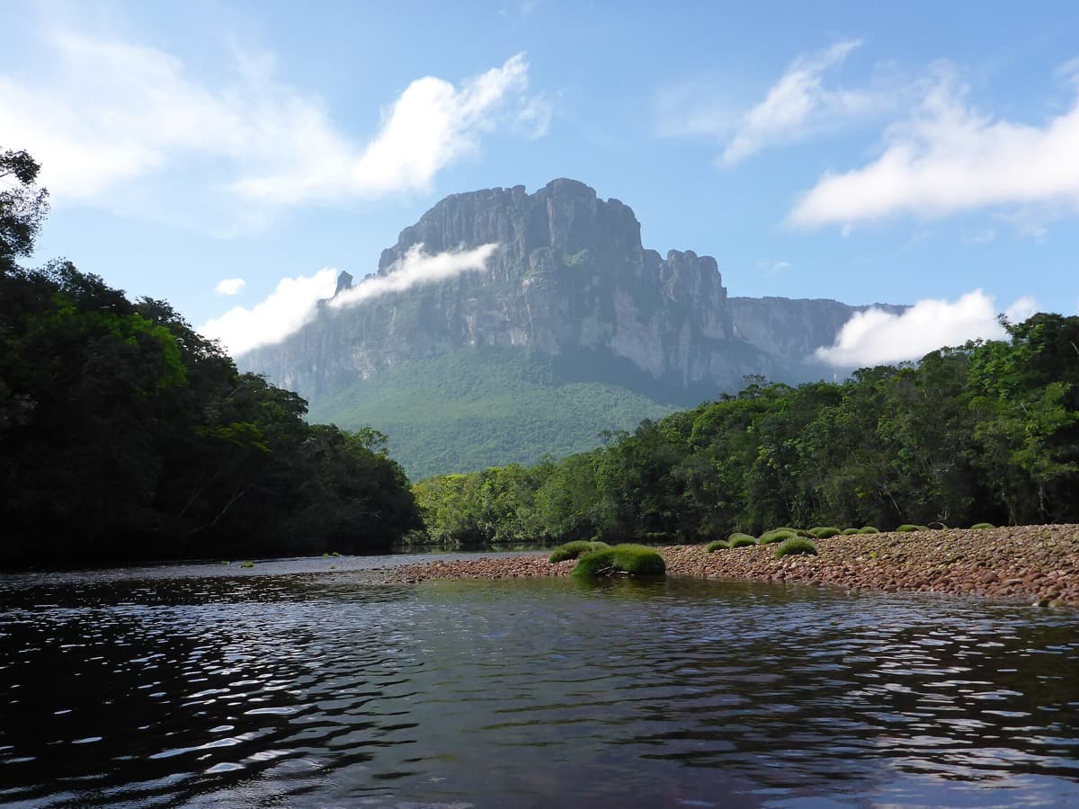A long sheer cliff face of a flat-topped mountain above forest and a river