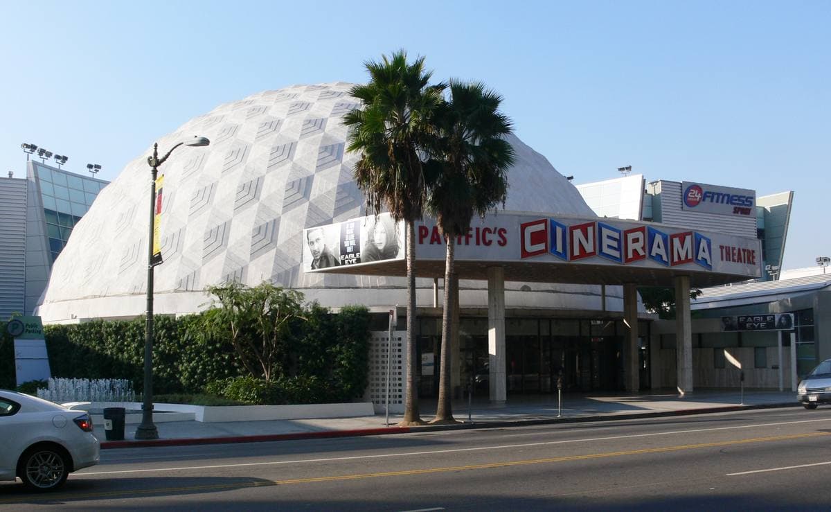 A white geodesic dome cinema with palm trees and a long marquee