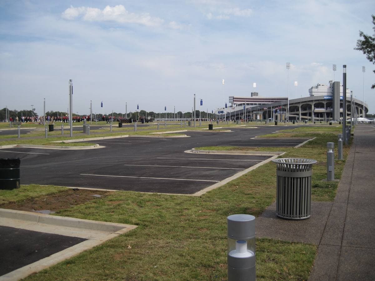 A wide lawn and paved lane leading towards a stadium under a grey sky