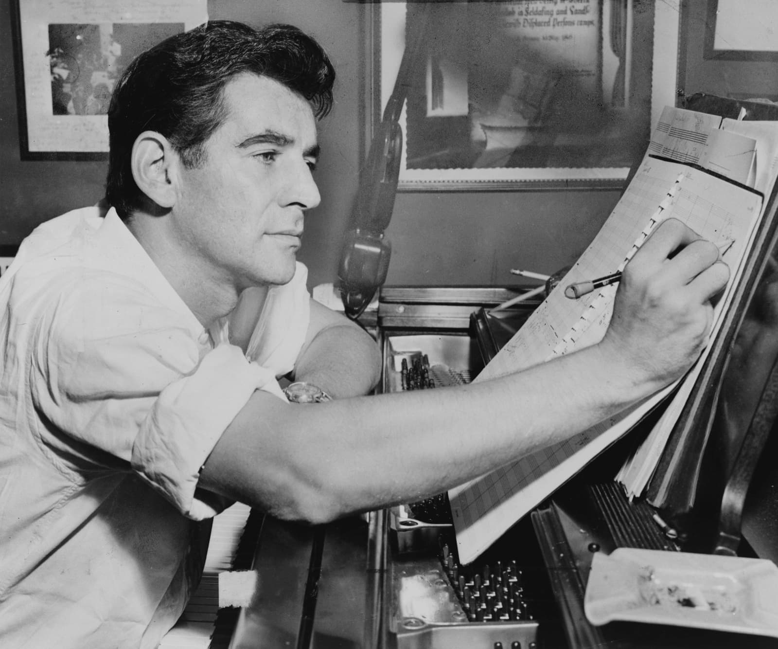 Leonard Bernstein seated at a piano writing on a music manuscript
