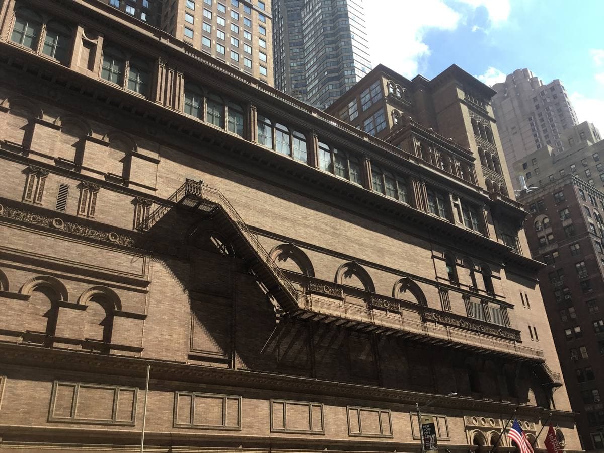 The brown brick and terracotta front of Carnegie Hall with towers rising behind