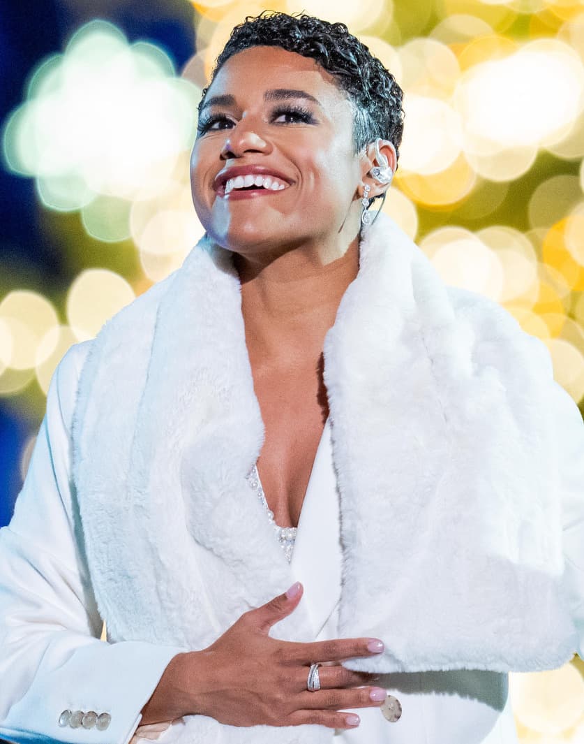 Ariana DeBose in a white fur wrap, laughing, lights behind her