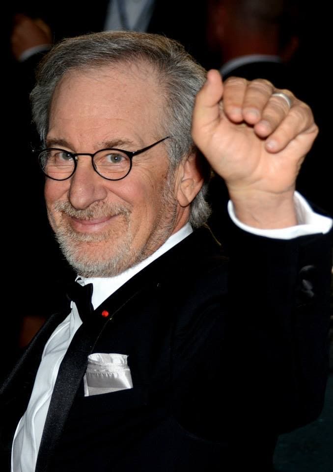 Steven Spielberg in round glasses and a dinner jacket, fist raised