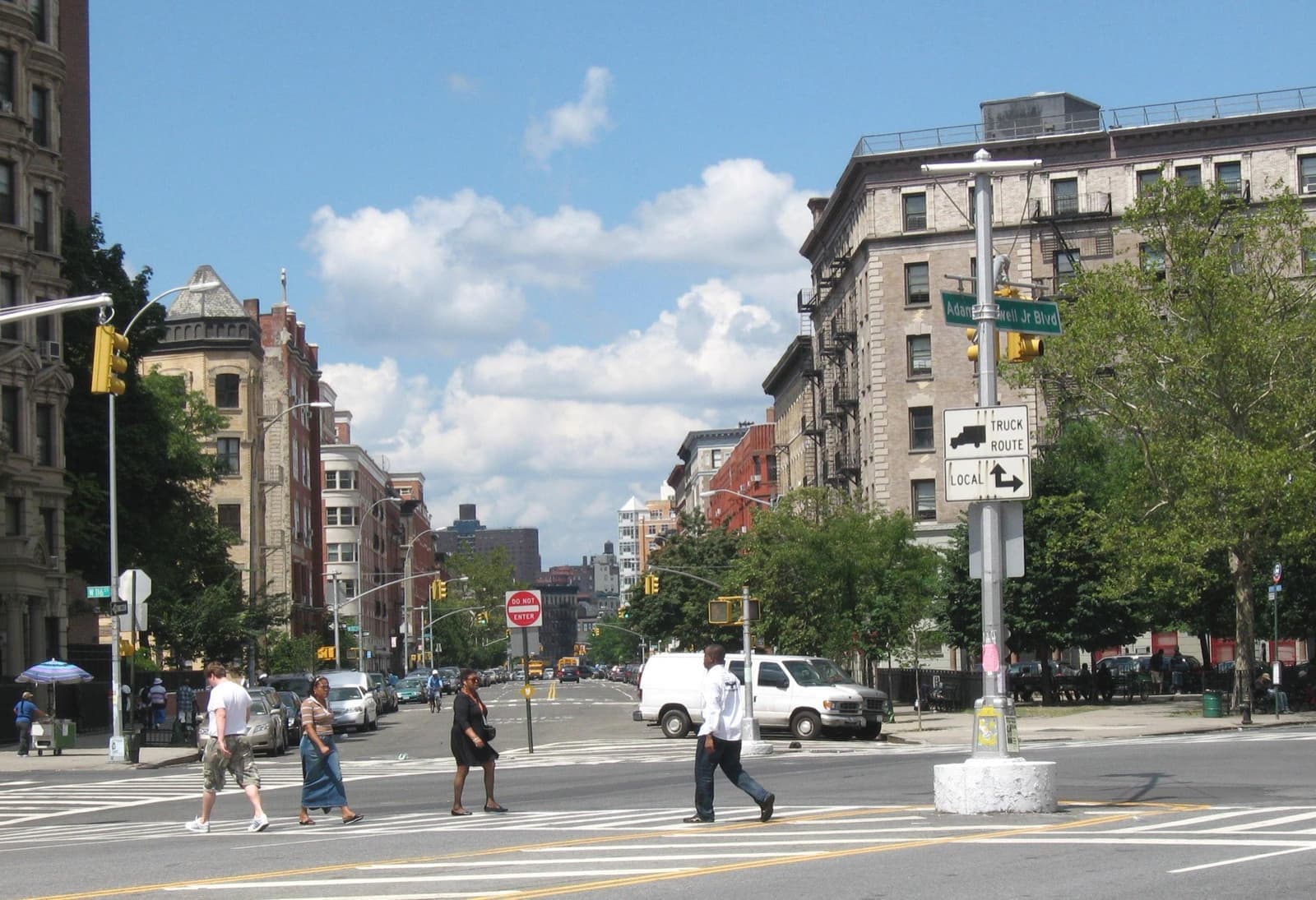 People crossing a Harlem avenue below pre-war apartment blocks
