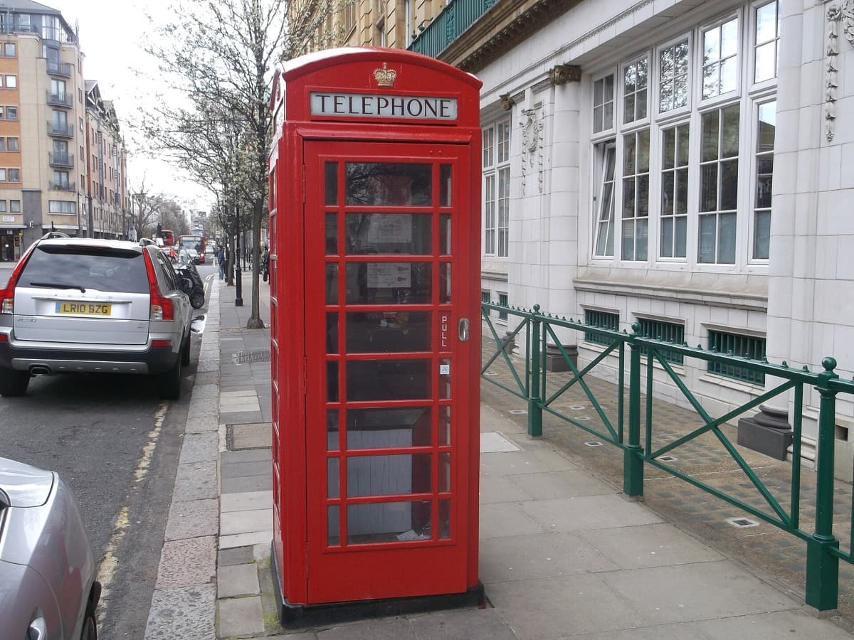 A tree-lined London street of tall stucco terraces with a red phone box