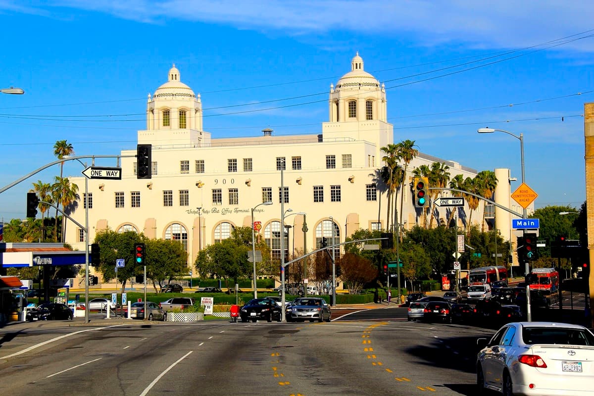A long cream-coloured 1940 post office building with a tall arched entrance and palm trees
