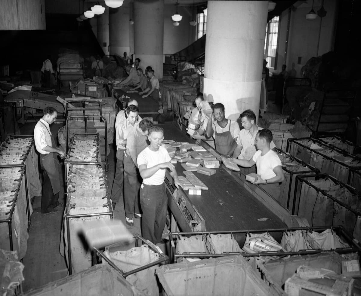 Men in shirtsleeves sorting parcels in a large post office hall