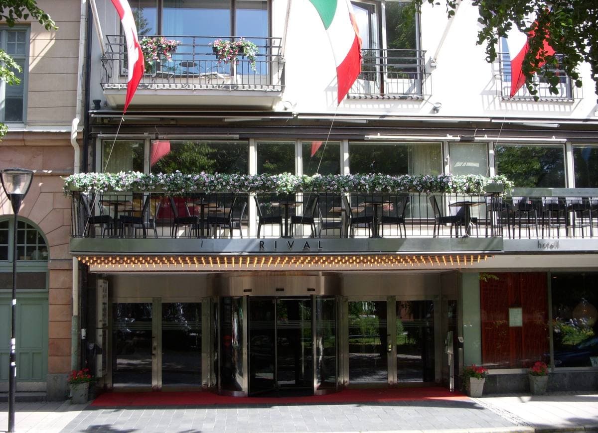 The entrance of a hotel with flags and window boxes above a red-carpeted doorway