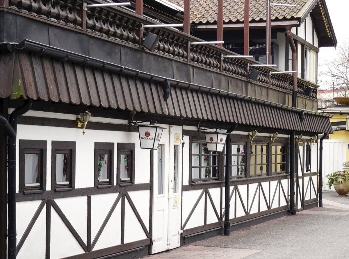 A long timber-framed building with a dark wooden balcony and lanterns, on a cobbled lane