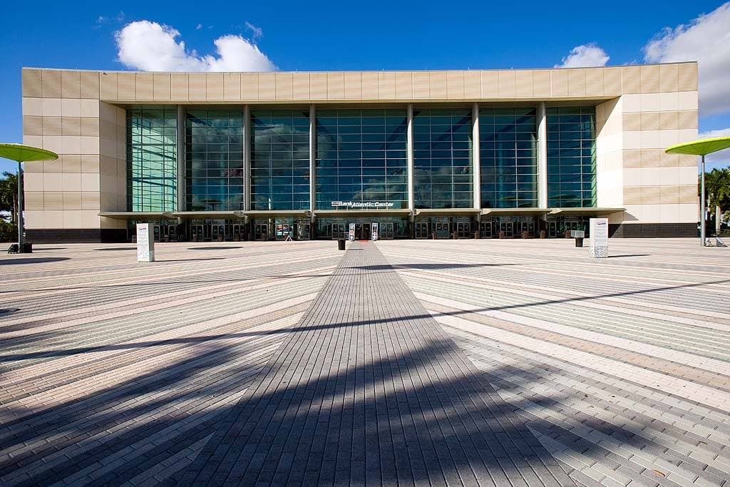 A large arena building with a curved glass entrance and a car park