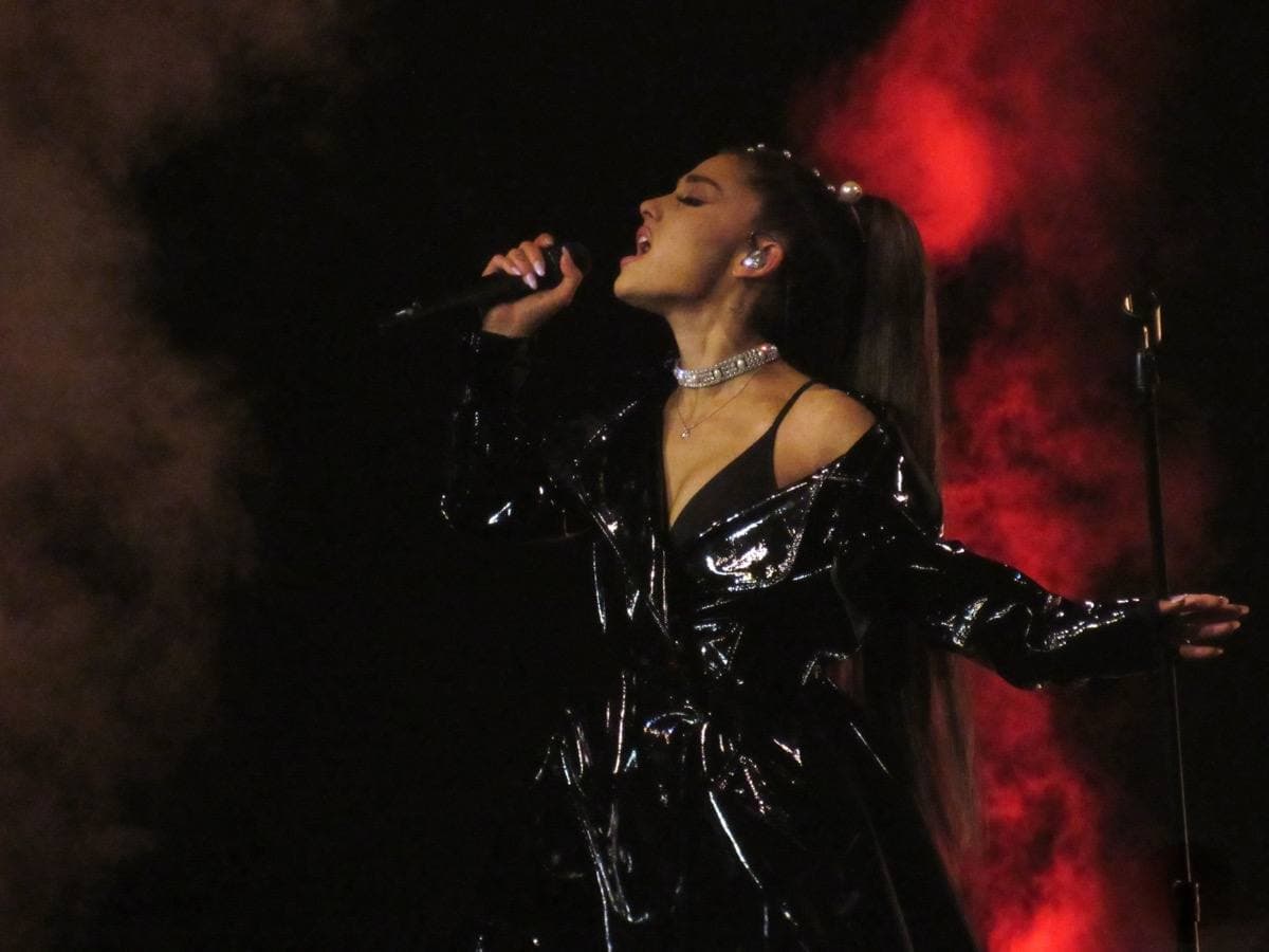 A singer in a pale outfit performing on a large stage under coloured light