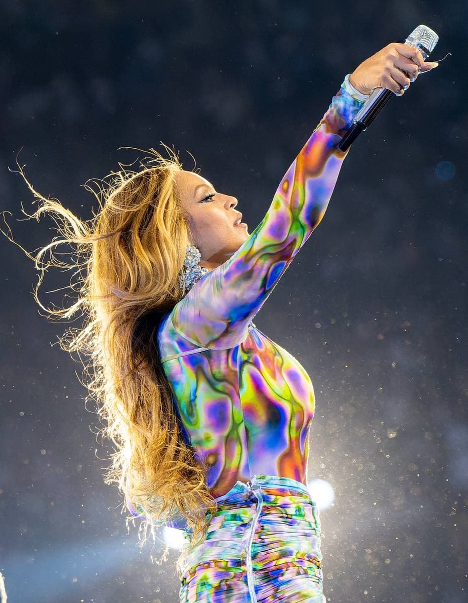 Beyoncé in profile, one arm raised with a microphone, her hair streaming out behind her in a wind
