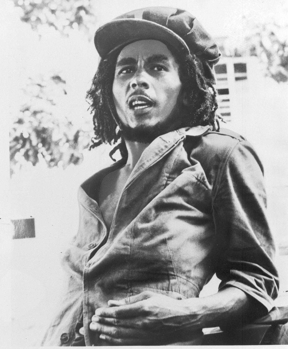 Bob Marley in a cap and denim shirt, sitting outdoors