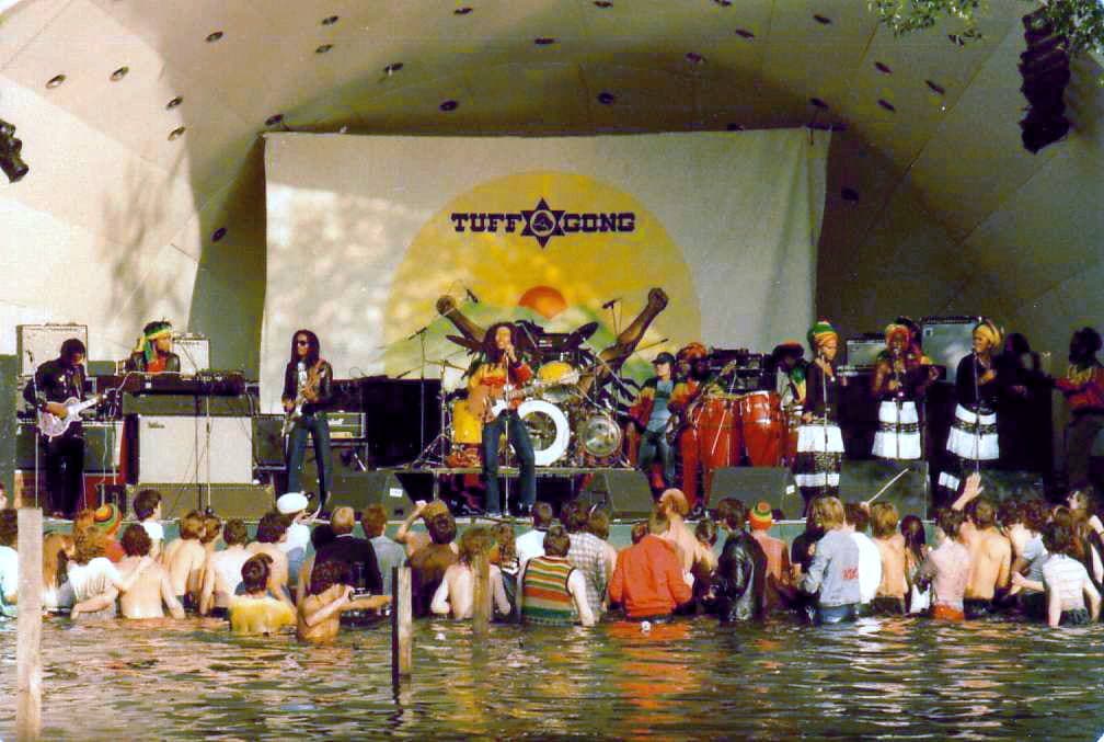The band on the Crystal Palace stage under a Tuff Gong banner, fans standing in the lake in front