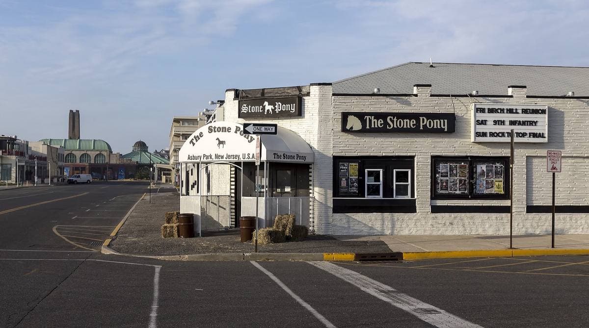A low white club building with black signs reading The Stone Pony on a wide, empty seafront street