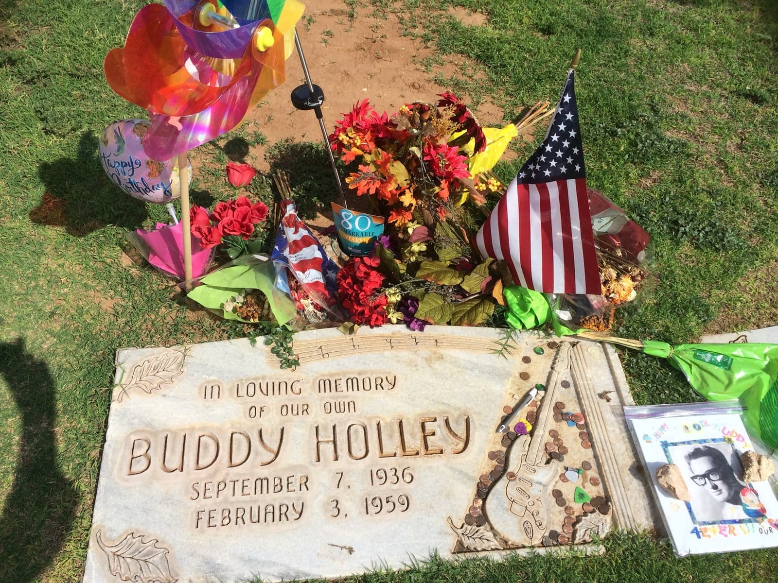 A flat granite grave marker carved with a guitar, with picks and tokens left on it