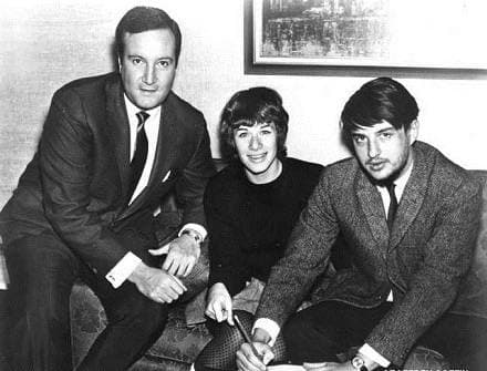 A man in a dark suit beside a young woman and a young man on a patterned sofa