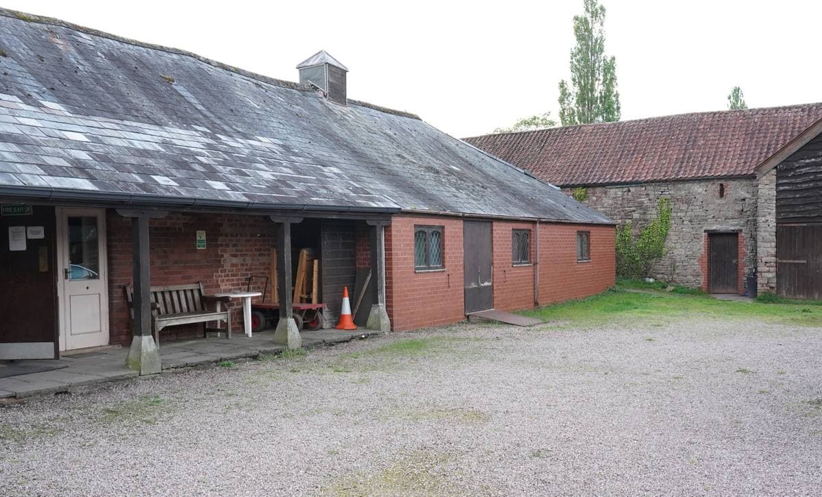A gravel yard in front of a long stone and brick range with a covered walkway
