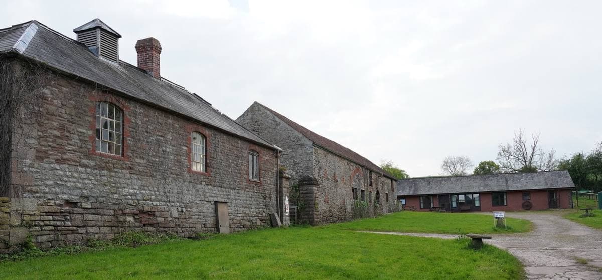 Long low stone farm buildings round a grassy yard under a pale sky