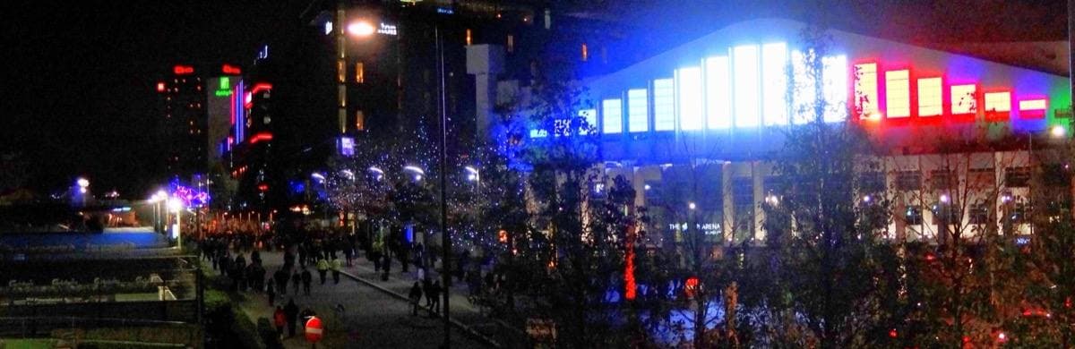 The lit front of Wembley Arena at night with a crowd outside