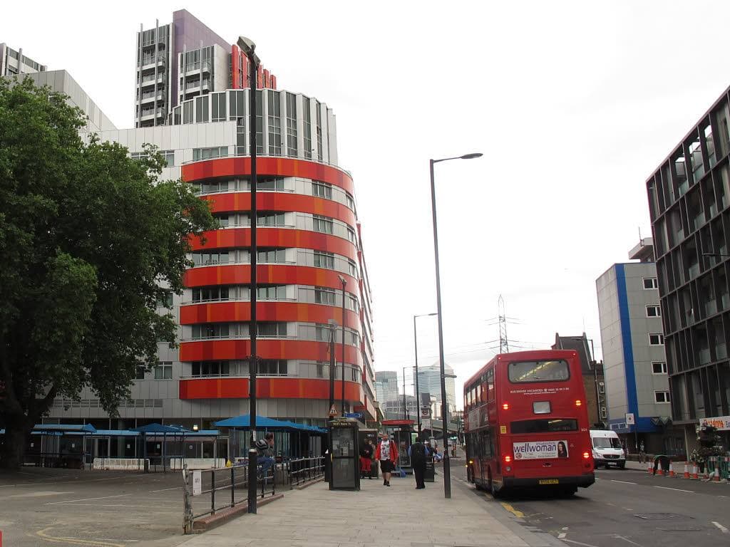 A busy main road with shops and flats under a grey sky