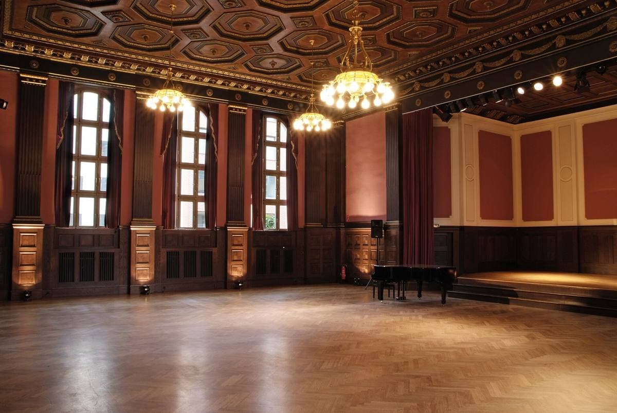 A tall panelled hall with chandeliers and a wooden floor, empty of people