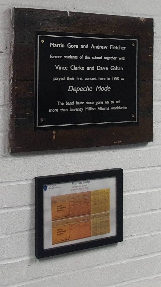 A framed plaque on a school wall above a framed old register page