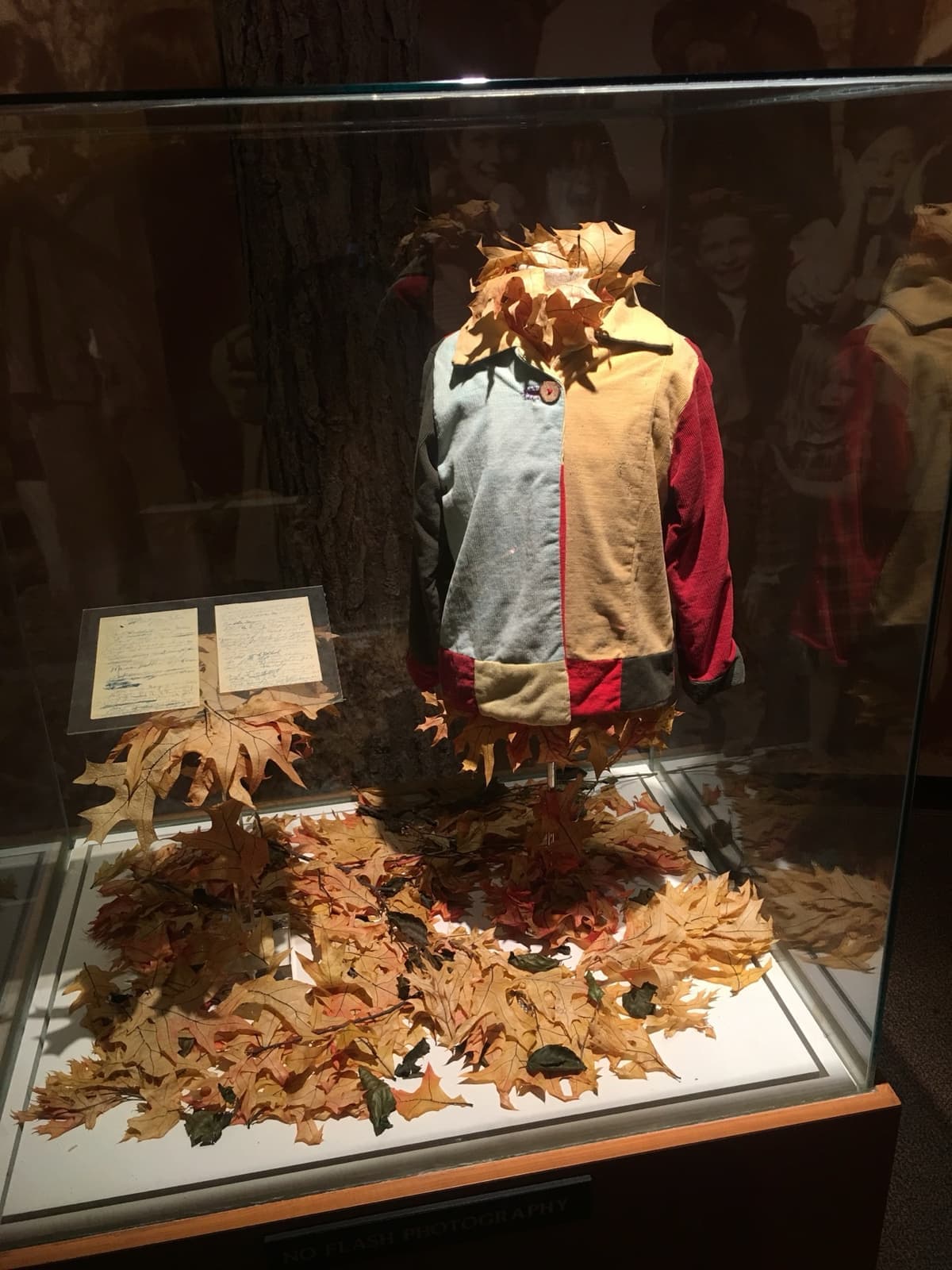 A small patchwork coat of bright fabric squares in a glass case