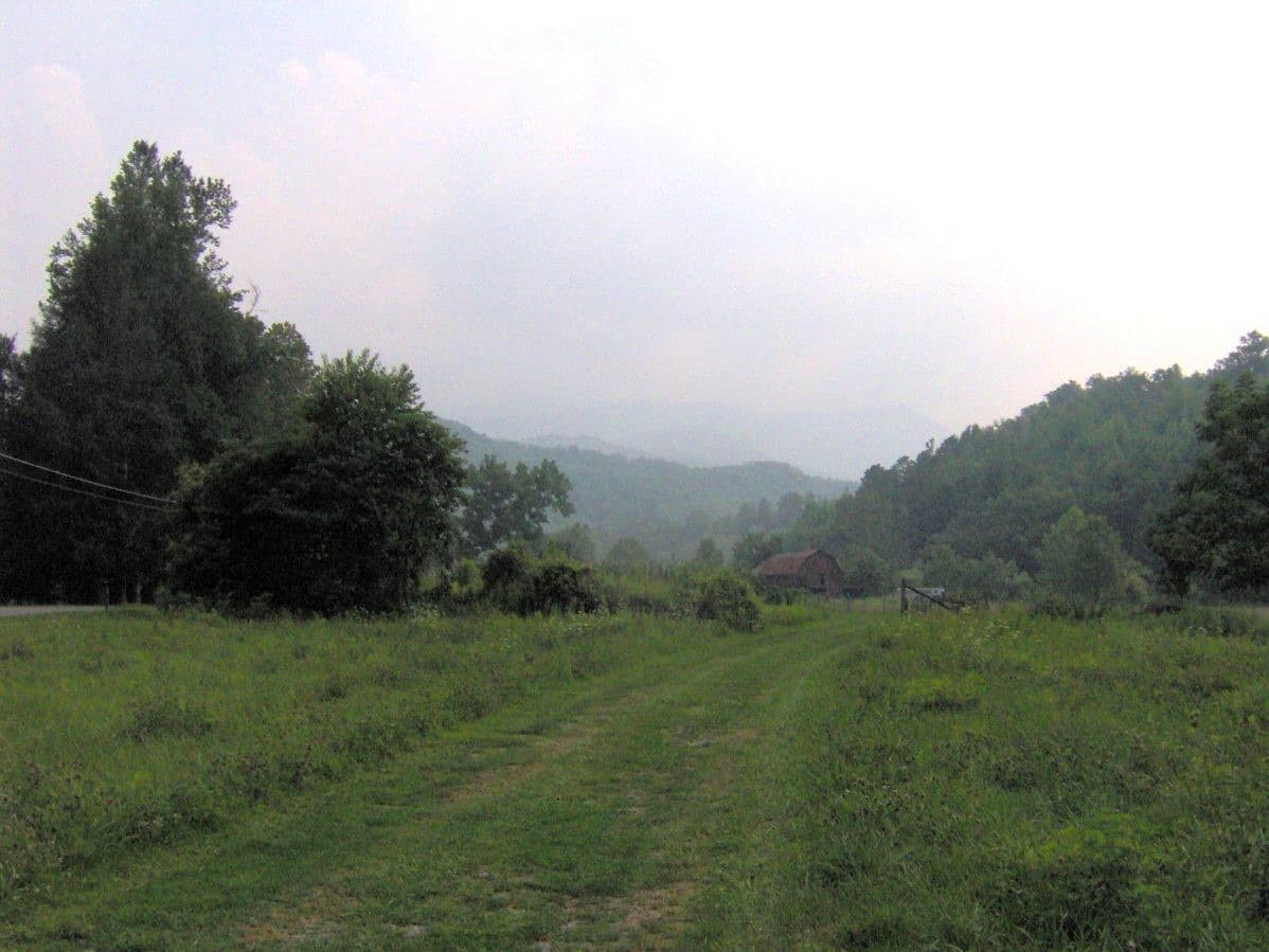 A cove of fields and woods below hazy mountains