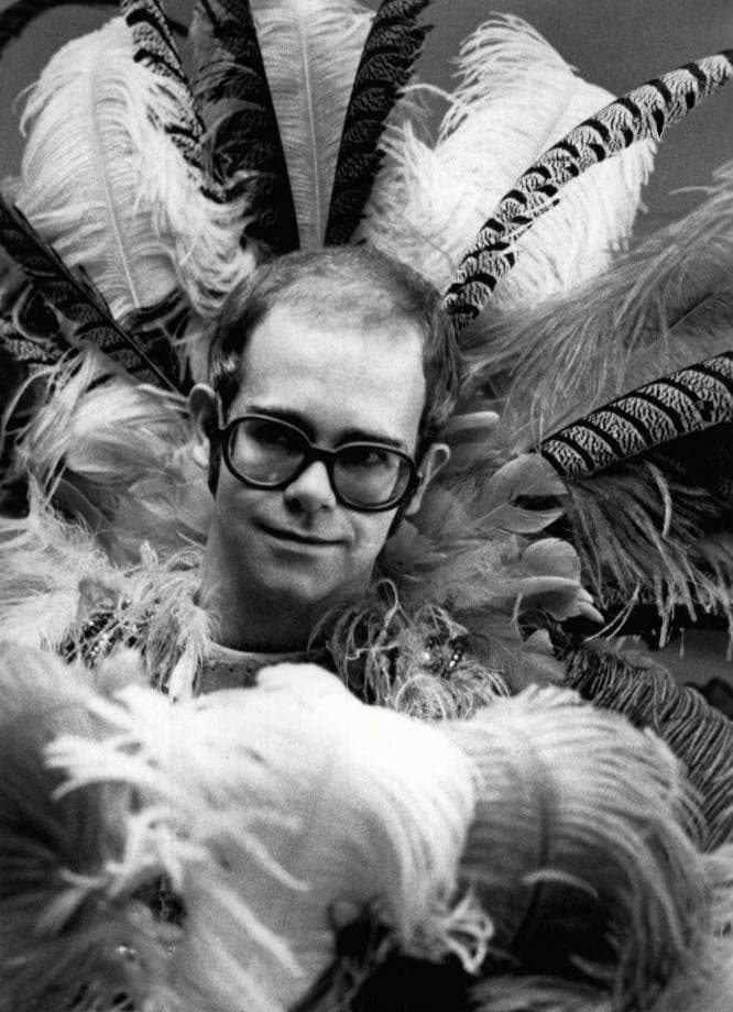 Elton John in large round glasses, framed by a huge fan of white feathers