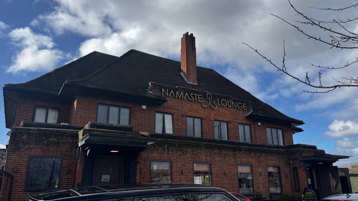 A large brick inter-war pub building with a dark tiled roof and a sign reading Namaste Lounge