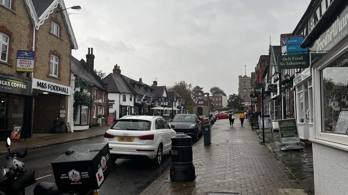 A narrow village high street of old timbered shops rising to a church tower on a grey day