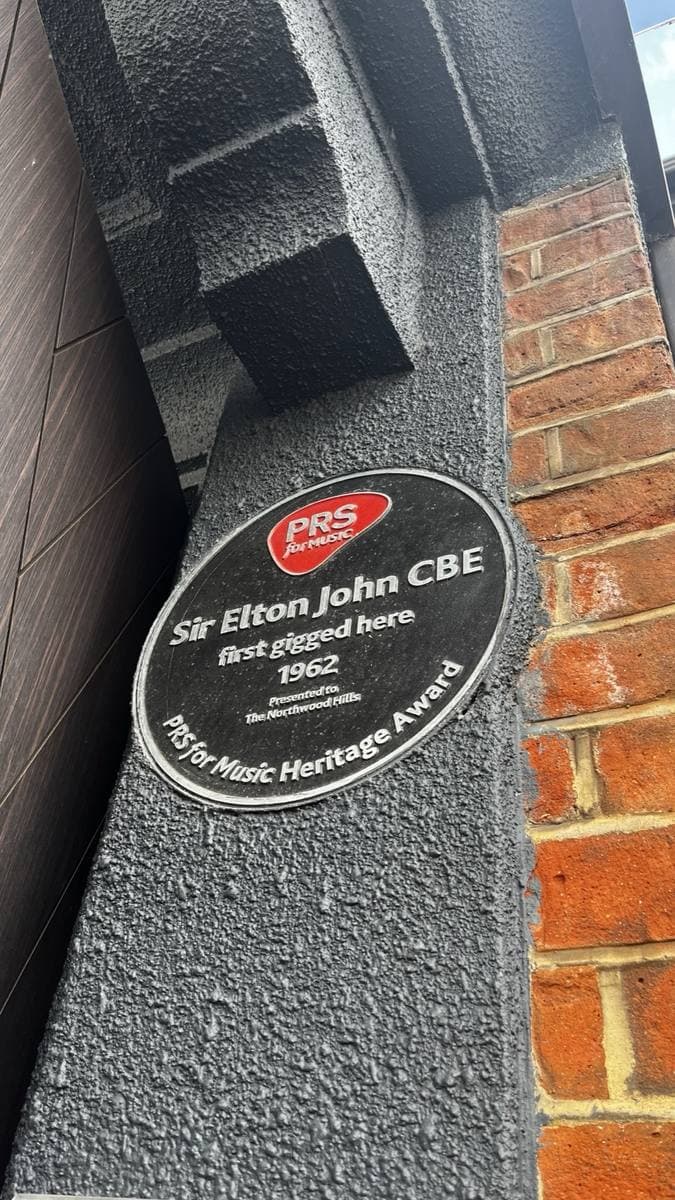 A round black plaque on a brick wall reading Sir Elton John CBE first gigged here 1962