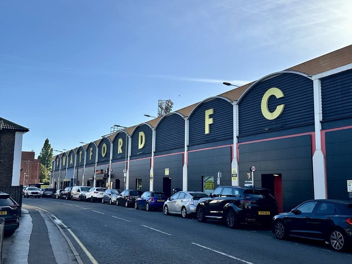 The curved navy and yellow bays of a football stand along a street, each bay carrying a letter of WATFORD FC