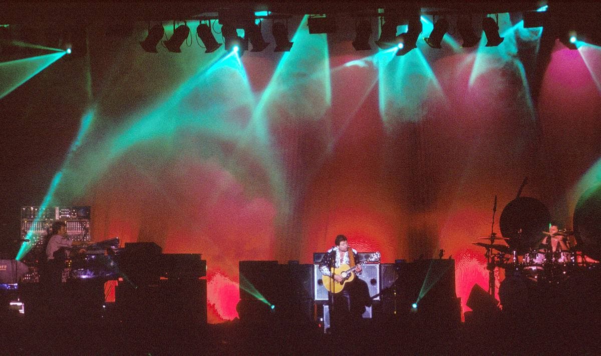 The trio on a lit stage, keyboards on the left and a drum kit behind