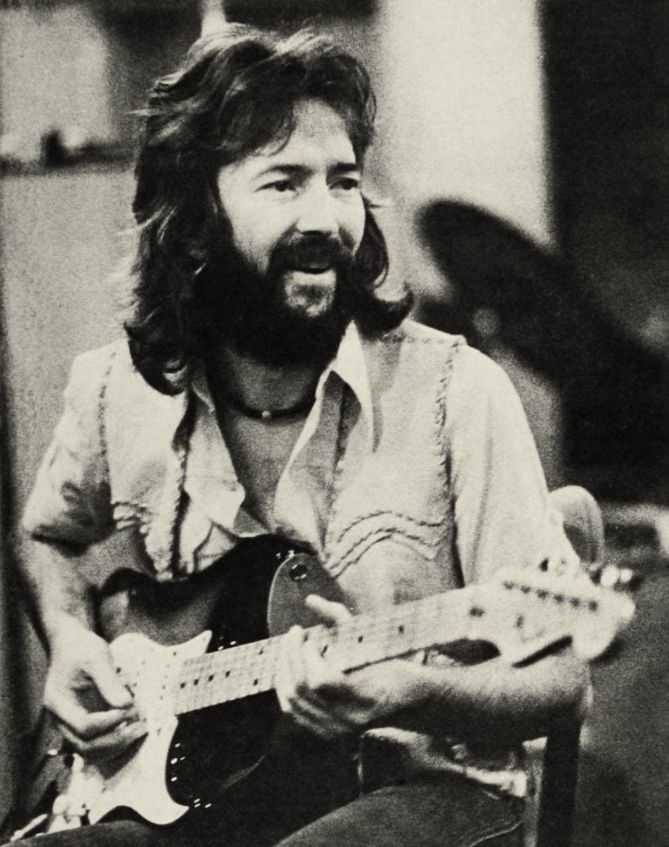 Eric Clapton, bearded and smiling, seated with an electric guitar