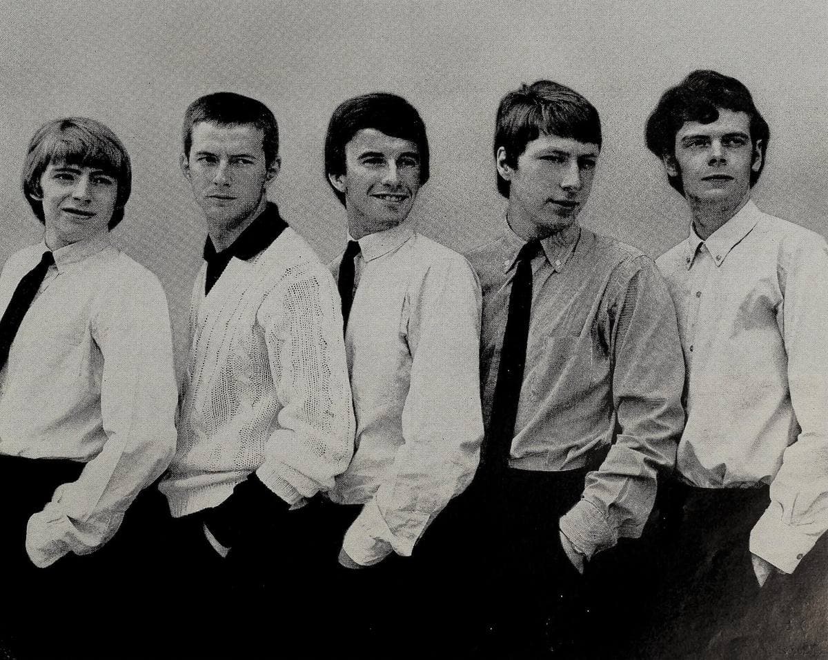 Five young men in white shirts and dark ties standing in a row